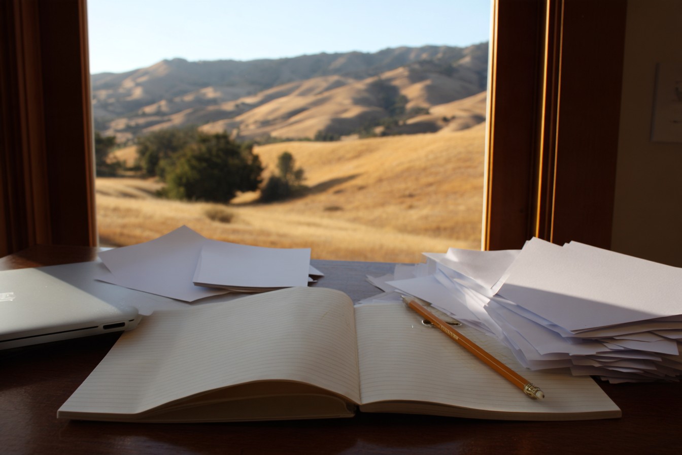 Illustrative image: papers and an open notebook on a desk facing golden California hills.