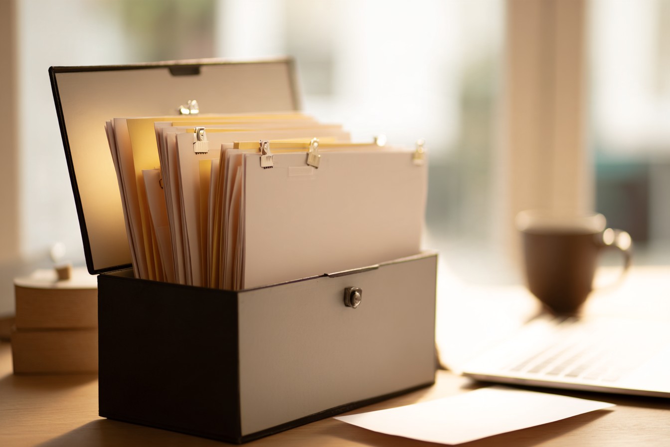 Illustrative image: an open records box of tabbed files on a desk in warm window light.